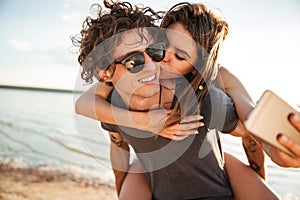 Young happy couple kissing and making selfie at the beach