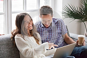 Young happy couple laughing watching funny video online on laptop