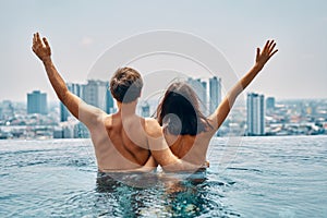 Young happy couple in love with arms up having fun in swimming pool