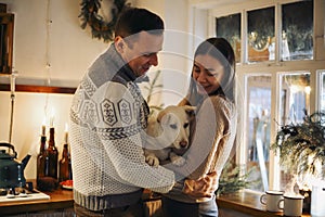 Young happy couple in love with cute little dog enjoying winter holiday season in cozy warm house