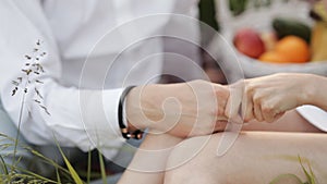 Young happy couple in love holding hands sitting on a meadow in a field through at sunset or sunrise. Romance