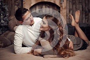 Young happy couple in love lying on rug in cozy wooden interior