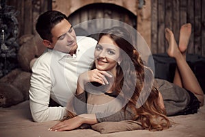 Young happy couple in love lying on rug in cozy wooden interior