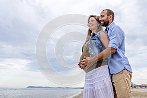 Young happy couple in love of a pregnant woman and her boyfriend hugging on the beach having fun on holidays. quality family time