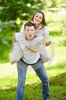 Young happy couple in love resting in nature. Woman jumped on man back, he spins her around, having fun.Concept of