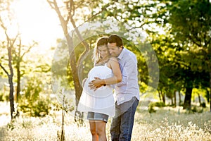 Young happy couple in love together on park landscape sunset with woman pregnant belly