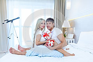 Young Happy Couple Lying In Bed, Hispanic Man Give Woman Surprise Present Envelope With Ribbon, Anniversary Celebration