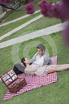 Young happy couple lying on a blanket together while having a picnic in the park, blossoms in the foreground