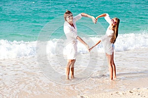 Young happy couple making heart shape at beach.