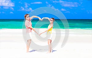 Young happy couple making heart shape on tropical
