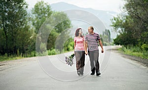 Young happy couple man and woman are walking along an empty road, the girl is holding a bouquet of flowers