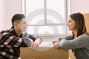 Young happy couple moving house looking each other leaning on a box