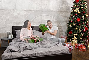 Young happy couple in pajamas rejoice at their presents while si