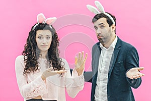 Young happy couple on the pink background. On the head is a rabbit ears. A young girl holding small carrots in surprise