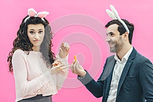 Young happy couple on the pink background. On the head is a rabbit ears. A young man holding a carrot of small size in