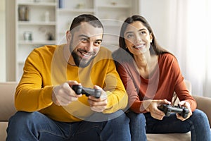 Young Happy Couple Playing Video Games With Joysticks At Home