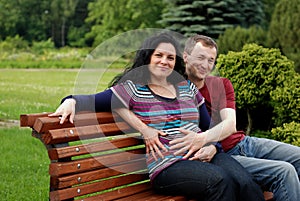 Young happy couple (pregnant woman) on bench