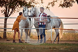 Young couple preparing their horses for a ride on  farm