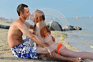 Young happy couple relaxing & kissing on sandy sea beach embracing