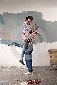 Young happy couple is repairing apartment and painting the wall at home. Loving couple is having fun while they are