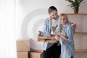 Young happy couple in room with moving boxes in new home, husband hugging wife celebrating mortgage