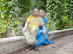 Young happy couple sits in the arbour twined greens