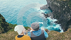 Young happy couple sitting on the edge of the mountain and looking to each others, romantic date on the beach.