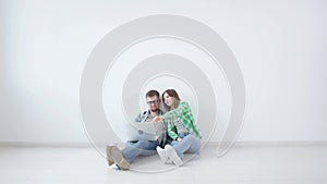 Young happy couple is sitting in an empty room and planning to arrange furniture in a new house