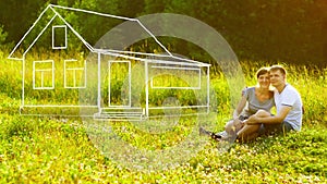 Young happy couple sitting on green grass in park and dreaming about they own house. Mortgage concept.