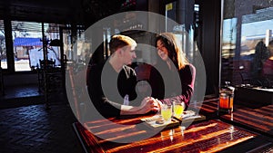 Young happy couple sitting near table with sea-buckthorn broth in cafe discussing film