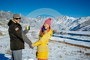 Young happy couple in snowy mountains with copy space. Guy and girl in bright clothes holding hands looking at camera and smiling