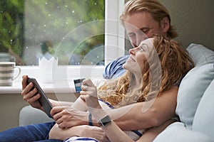 A young happy couple snuggling while using a digital tablet to make online card payments. A young happy couple snuggling