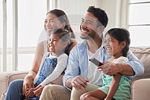 Young happy couple spending quality time with their children on a weekend and watching tv while sitting on the couch at