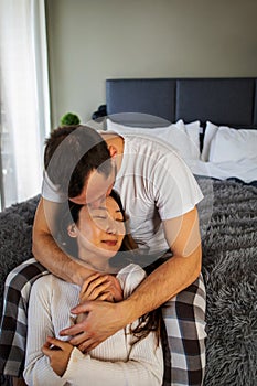 Young happy couple spending time at home, sitting on bed in cozy renovated apartment, laughing, having fun