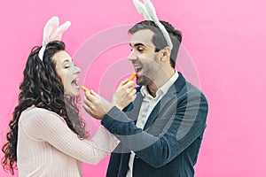 Young happy couple standing on pink background. On the head of the ears of the bunny. During this man and his wife