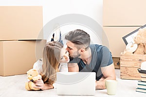 Young happy couple with tablet PC and moving boxes sitting on floor at new home