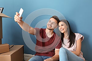 Young happy couple taking selfie with moving boxes at new home