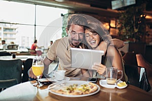 Young happy couple using digital tablet and eating pizza in a restaurant. Selective focus