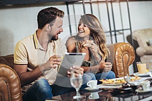 Young happy couple using digital tablet and eating pizza in a restaurant. Selective focus