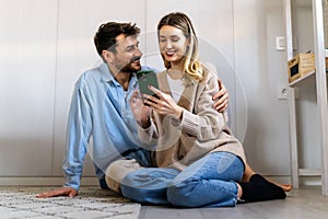 Young happy couple using phone to share social media news at home, doing shopping online.