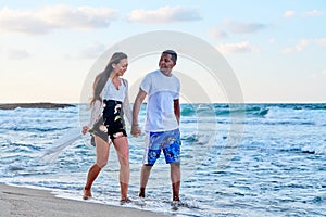 Young happy couple walking on the beach holding hands, copy space