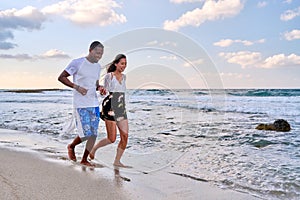 Young happy couple walking on the beach holding hands, copy space