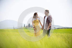 A young happy couple walking on a green meadow holding hands