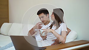 Young happy couple watching movie together in white soft sofa, drinking coffee