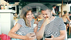 Young happy couple watching photos on the smart phone in a cafe