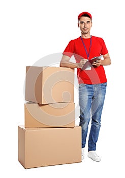 Young happy courier with clipboard near pileof  boxes on white background