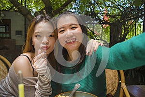 Young happy and cute Asian Chinese girlfriends taking selfie portrait picture with mobile phone camera for using on internet