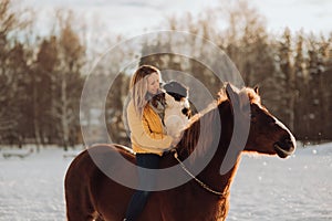 Young happy cute smiling woman with her dog border collie sit on horse in snow field on sunset. yrllow dress