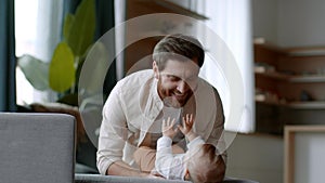 Young happy dad playing with his newborn baby daughter, blowing at her, carefree girl laughing, empty space
