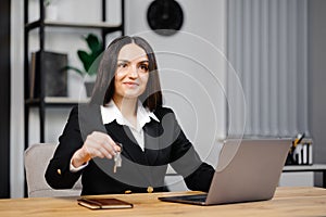 Young happy employee business woman wearing suit sitting at office desk with laptop and giving key in office